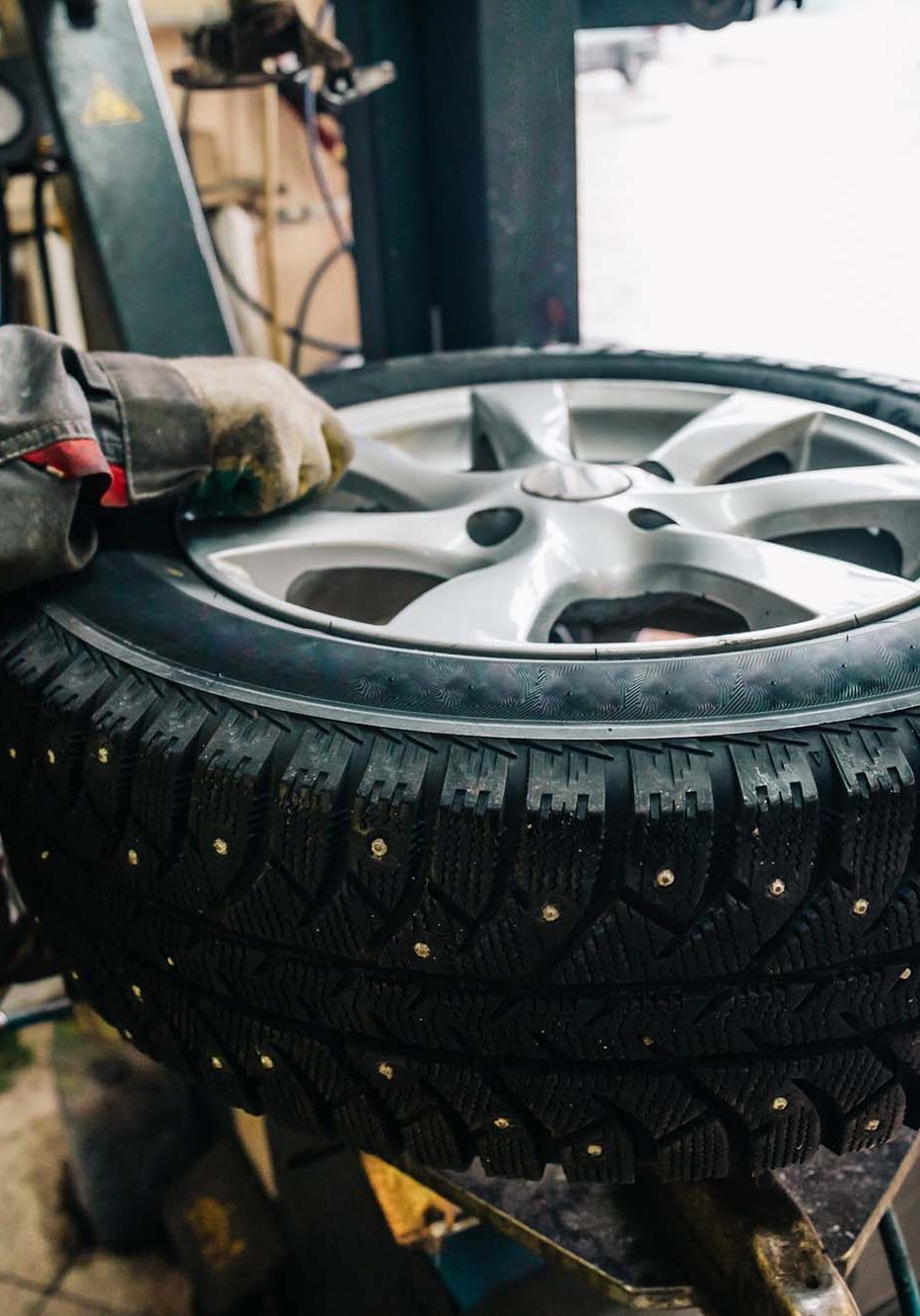 Car mechanic worker doing tire replacement and wheel balancing with special equipment in repair service station, toned